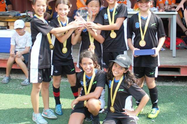 A celebratory group of Green Valley students smiling and holding a trophy together after a sports event
