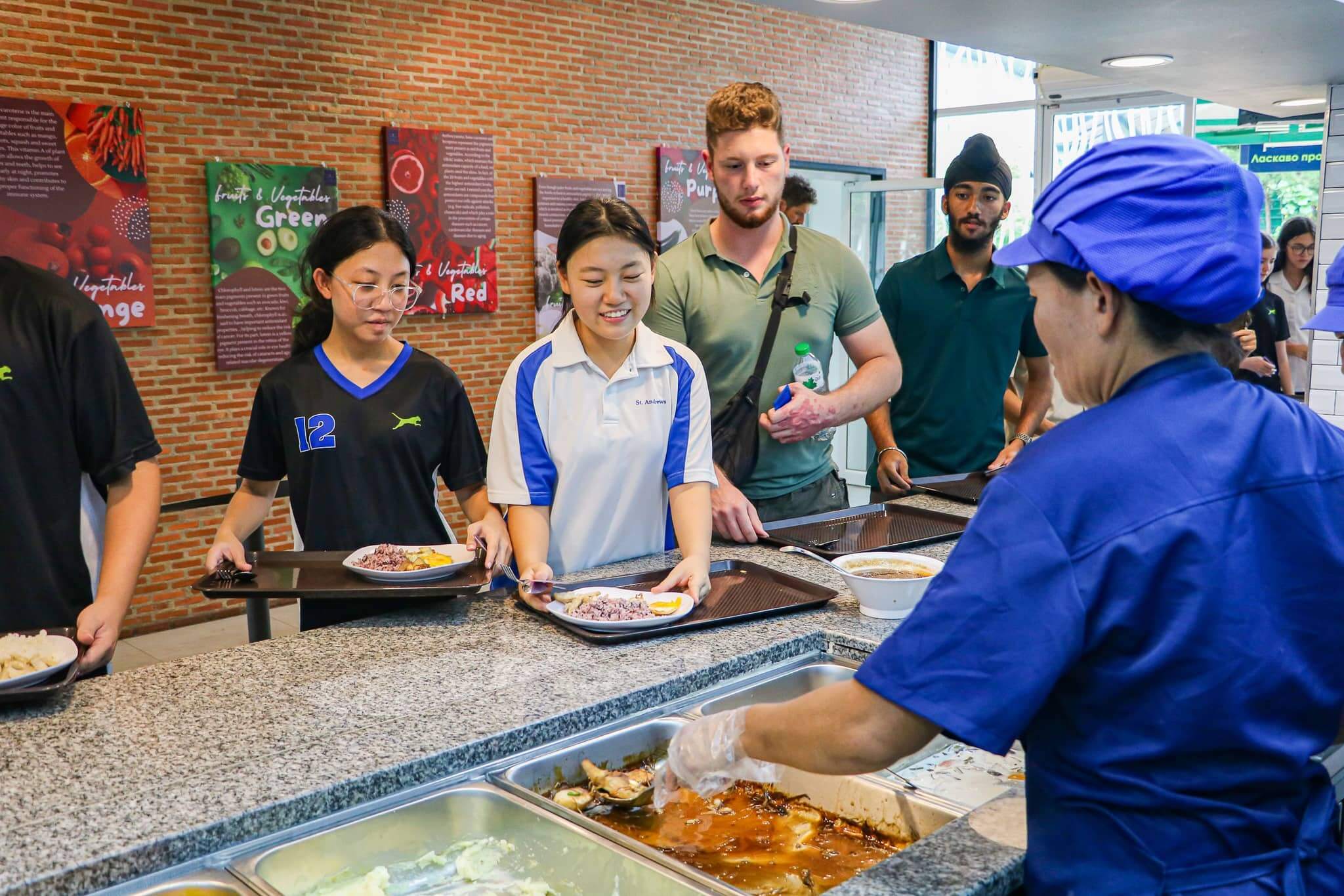 Happy students queue for healthy international school lunch while staff serves food in a clean canteen