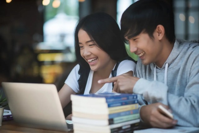 ib-school Students smiling while using a laptop for higher education planning.