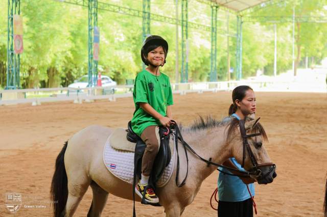 riding-horse-at-school Student smiling while riding a horse at the school's nearby outdoor riding facility, part of extended sports programme