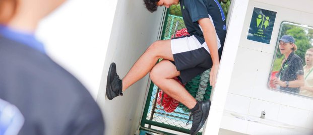 Student climbing during a school physical challenge while teachers cheer supportively, encouraging confidence and exploration in sport