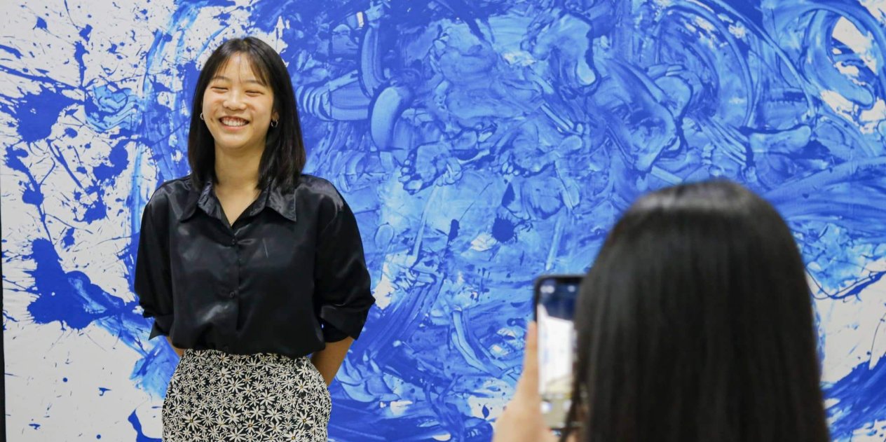 A student smiles in front of her abstract art project, expressing creativity and confidence nurtured through the IBDP’s balanced academic and artistic structure.