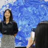A student smiles in front of her abstract art project, expressing creativity and confidence nurtured through the IBDP’s balanced academic and artistic structure.