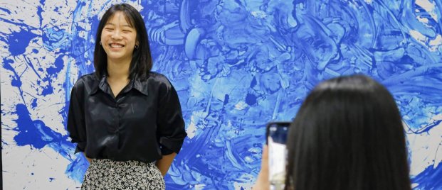 A student smiles in front of her abstract art project, expressing creativity and confidence nurtured through the IBDP’s balanced academic and artistic structure.