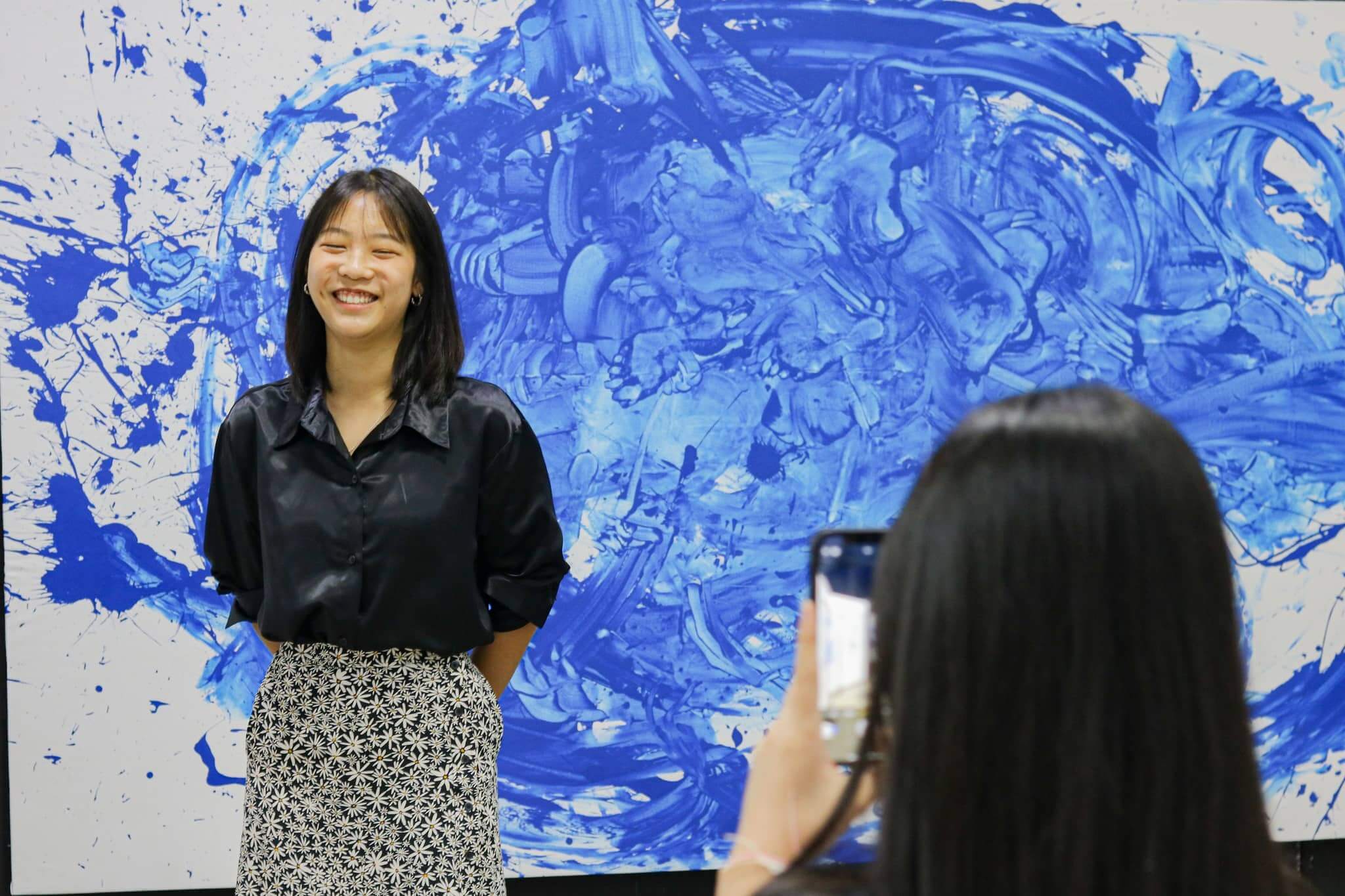 balanced-academic A student smiles in front of her abstract art project, expressing creativity and confidence nurtured through the IBDP’s balanced academic and artistic structure.