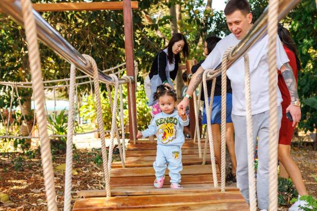 Young child crosses a wooden bridge with support from a parent, building confidence through encouragement, exploration, and shared success.