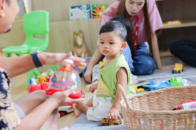 Young child explores toys with focused attention during play-based activity, supported by adults in a nurturing learning environment.