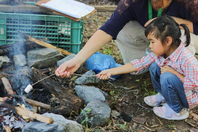 eco-experiences A preschooler at St. Andrews Green Valley roasts marshmallows during Forest School, learning safe fire management and building early environmental awareness through hands-on eco experiences in eco school for preschoolers.