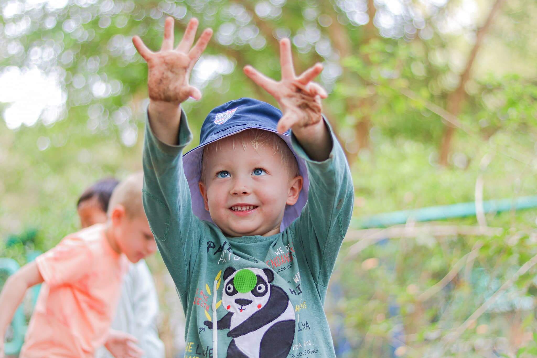 A smiling preschooler at St. Andrews Green Valley proudly shows muddy hands after outdoor play, developing confidence, self-regulation, and resilience through nature-based learning in eco school for preschoolers.
