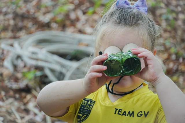 A Forest School student at St. Andrews Green Valley explores nature using handmade binoculars, developing curiosity, creativity, and independent exploration through long-term child-led forest school experiences.