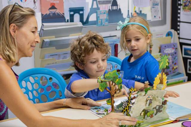 Two young children engage in storytelling and imaginative play with a 3D book, guided by a teacher who encourages creative thinking development