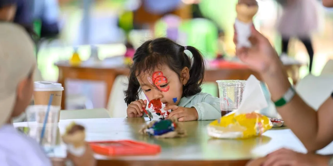 Young girl focuses intently on painting during a hands-on activity, expressing creativity and exploring her interests through open-ended materials.