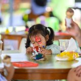 Young girl focuses intently on painting during a hands-on activity, expressing creativity and exploring her interests through open-ended materials.