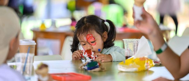 Young girl focuses intently on painting during a hands-on activity, expressing creativity and exploring her interests through open-ended materials.