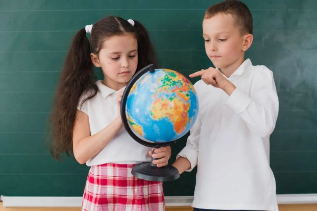 Children exploring a globe in the classroom, learning the 5 characteristics of a global citizen.
