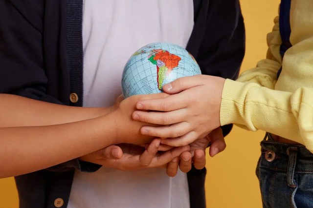 Children holding a globe together, representing the importance of becoming a global citizen.